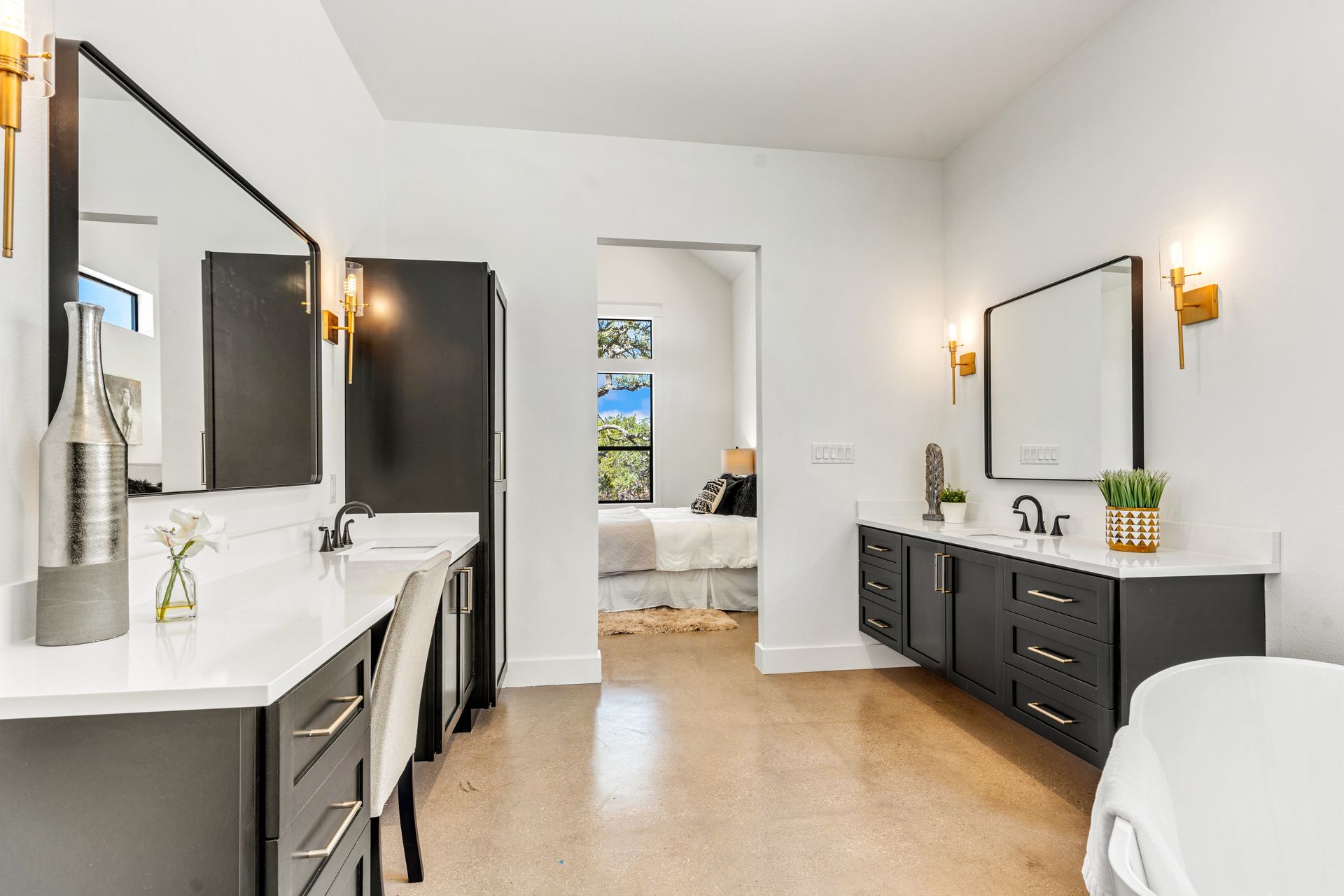 Modern bathroom with dark gray vanities, white countertops, large mirrors, and gold sconces.
