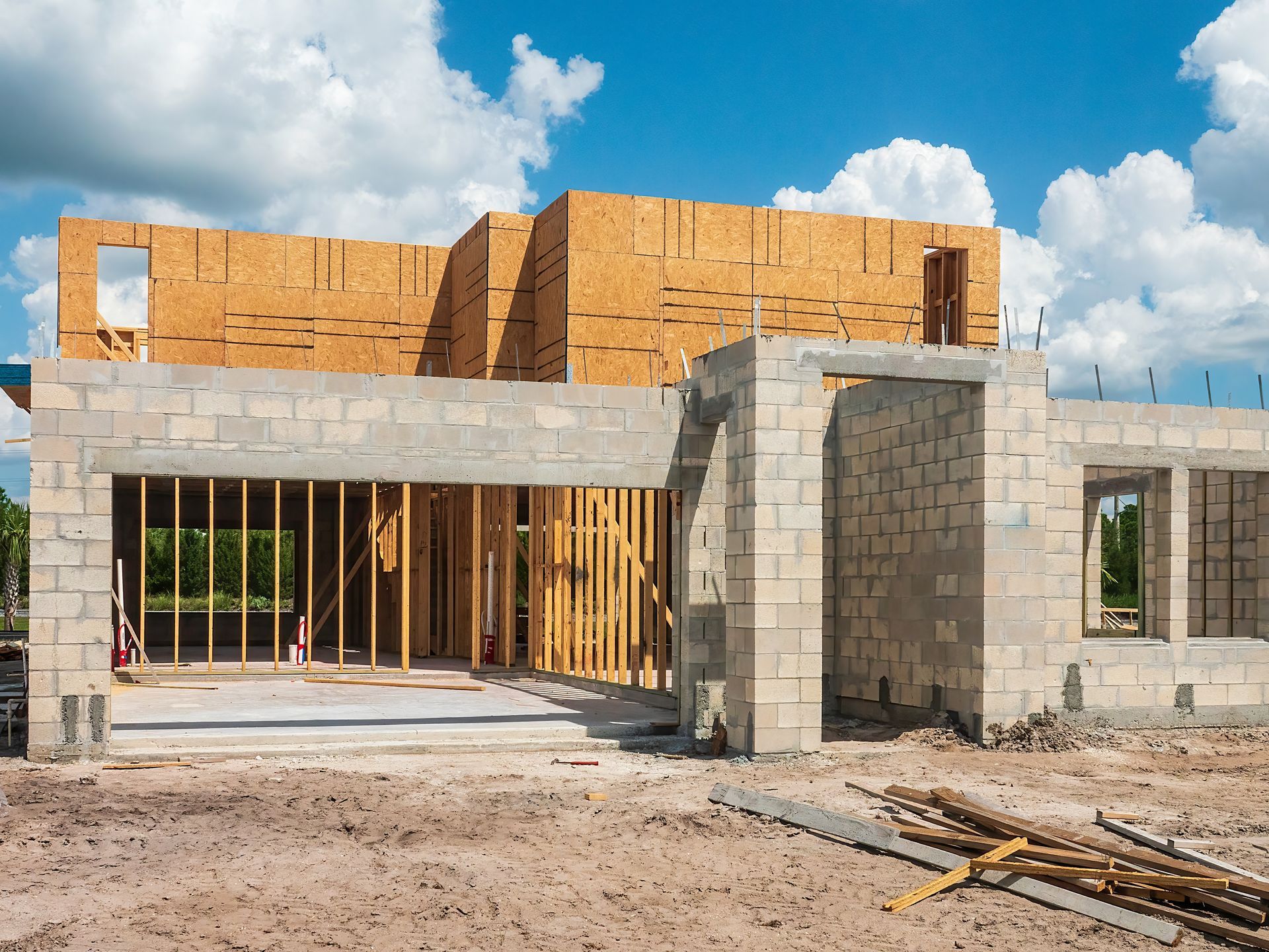 Construction site of a house; concrete block base and wood frame upper level under a blue sky.