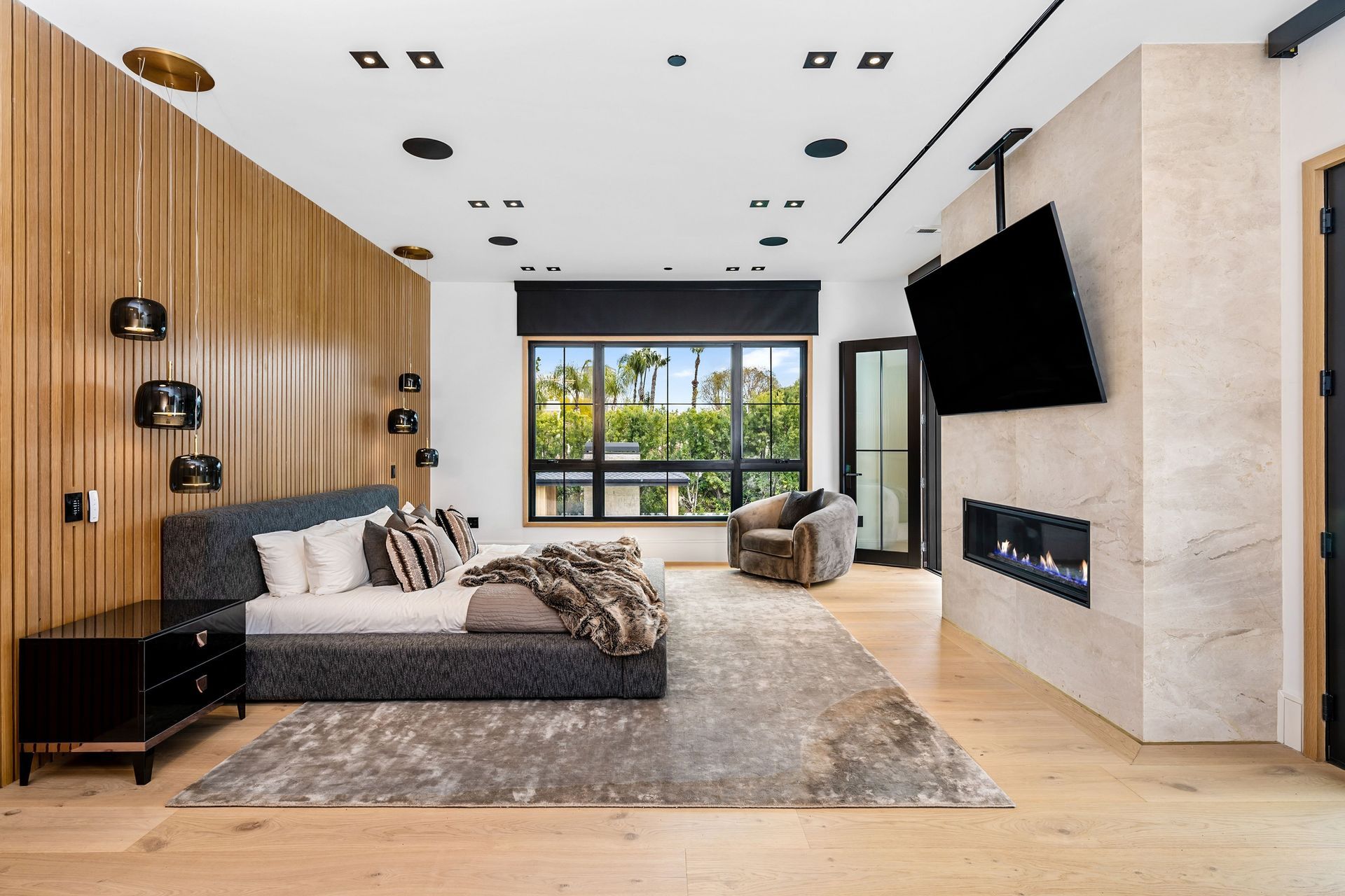 Luxurious bedroom with wood paneling, a fireplace, and a large window overlooking greenery.