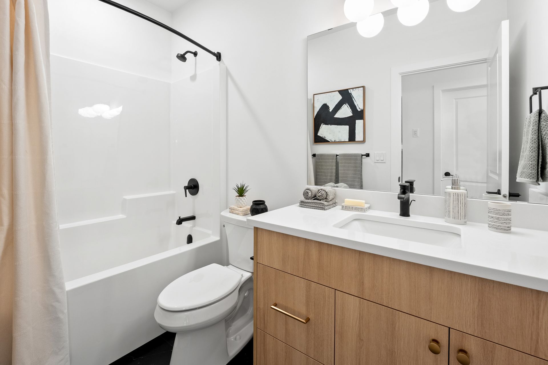 Modern bathroom with white walls, wood vanity, black fixtures, and a shower/tub.