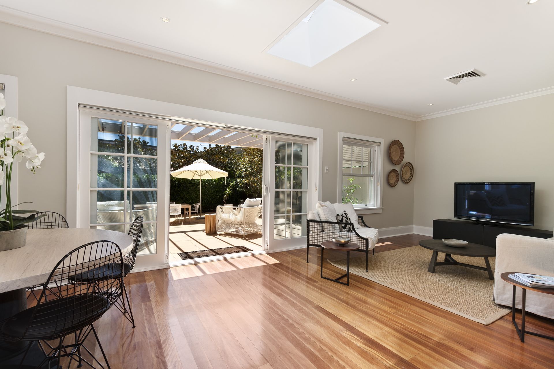 Bright living room with open doors to a patio. Hardwood floors, white walls, and contemporary furniture.