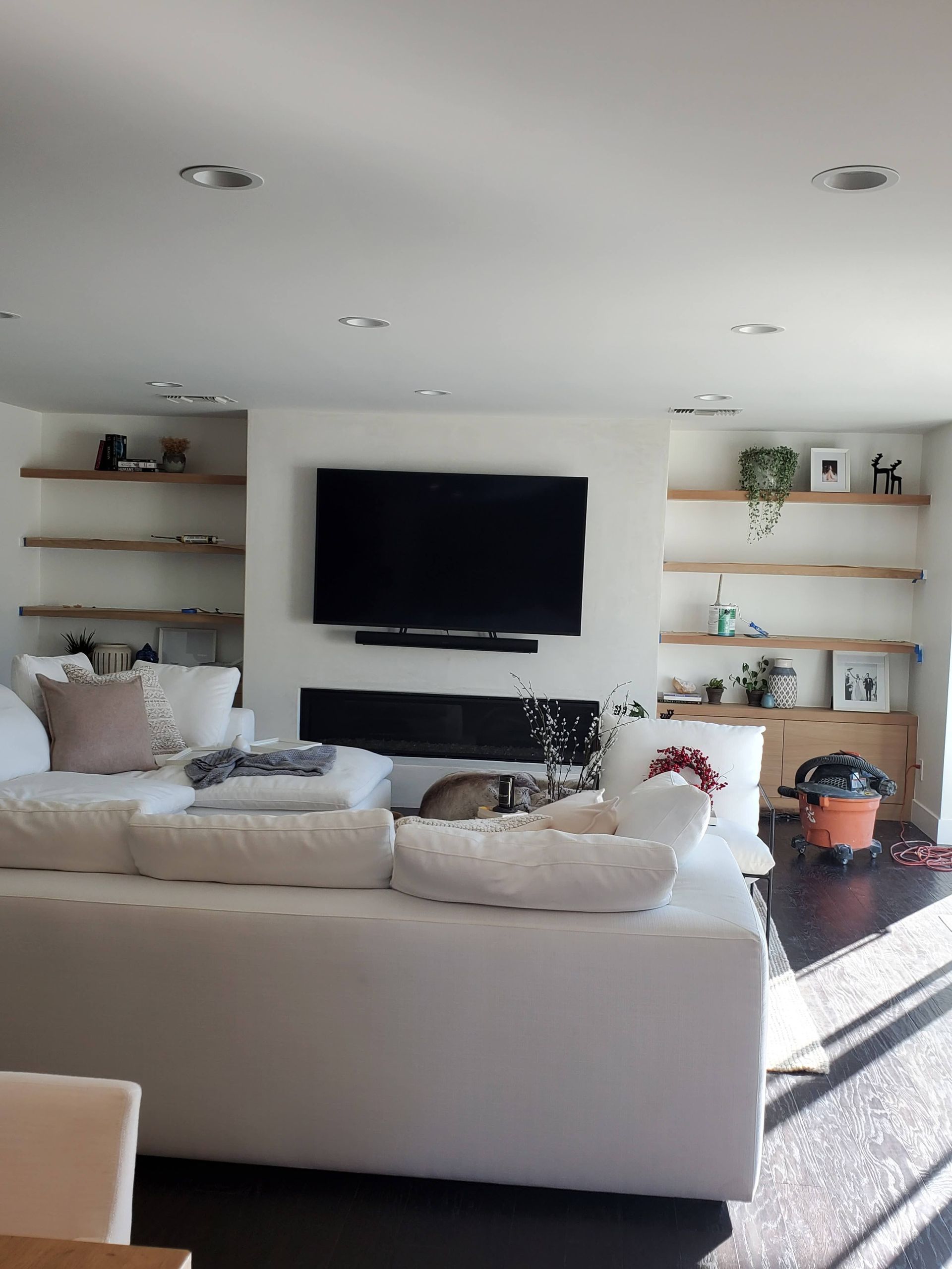 Bright living room with white sofa, TV above fireplace, and wood shelving.