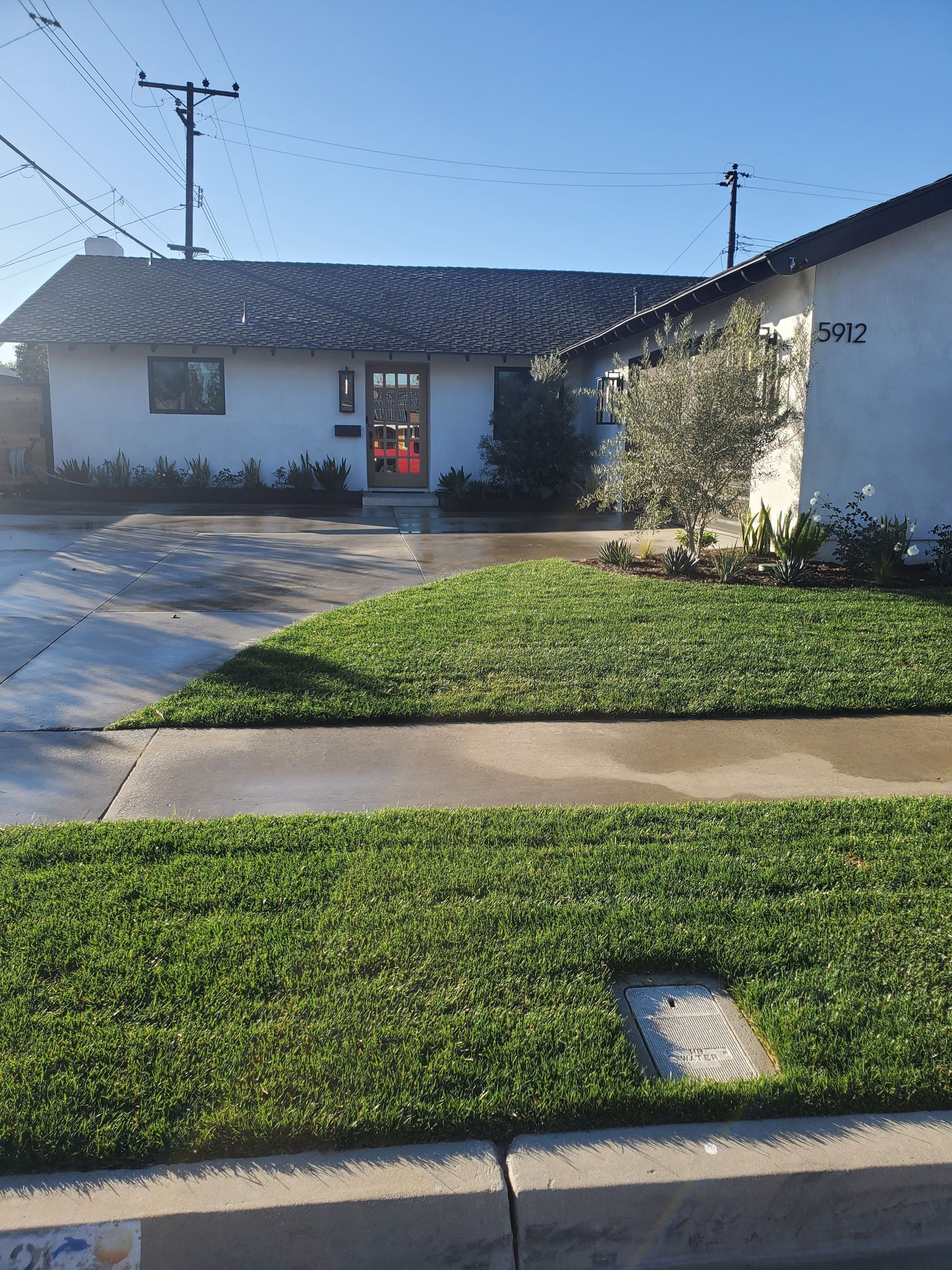 White house with green lawn, sidewalk, and street. A sunny day.