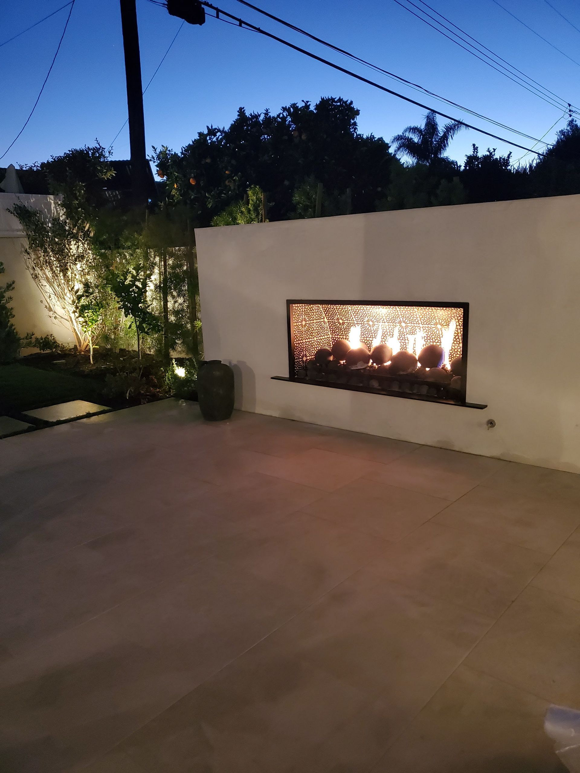 Outdoor patio at dusk with a lit fireplace set into a white wall.