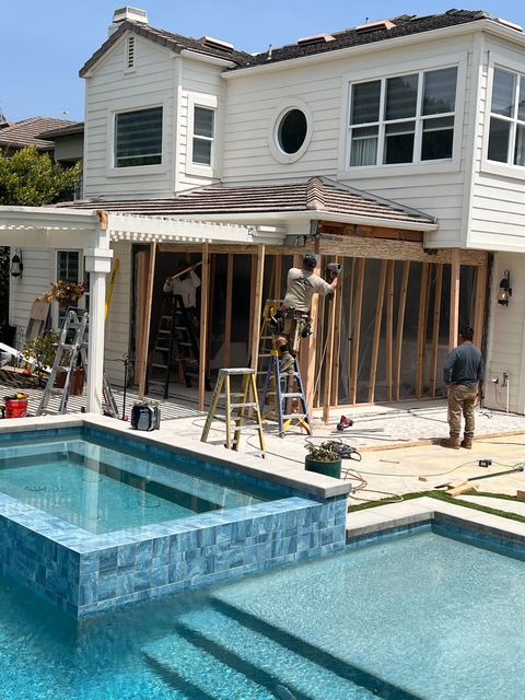 Construction workers building a structure adjacent to a pool at a white house with a blue tile pool.
