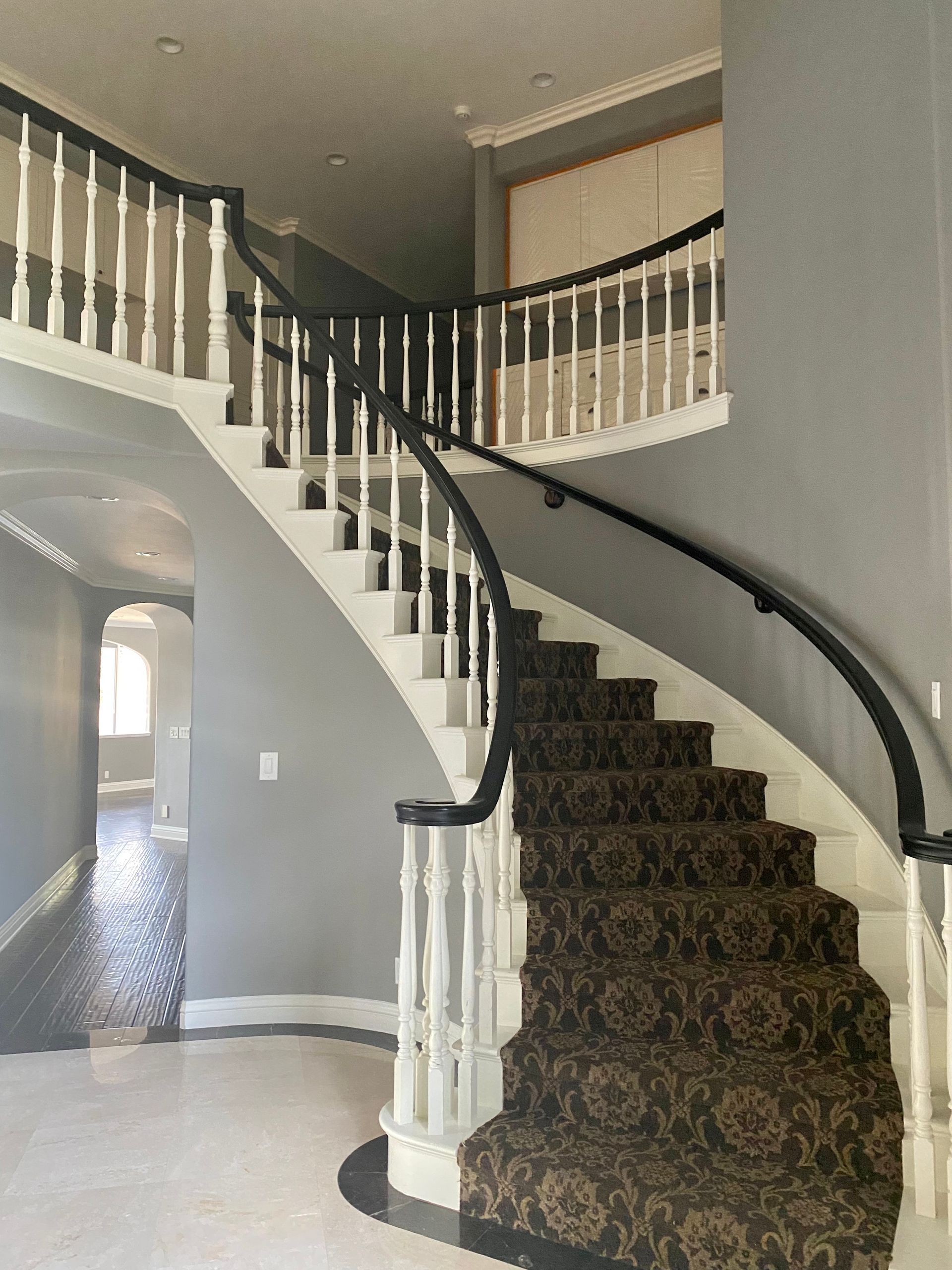 A grand staircase with carpet and black and white railing in a gray-walled entryway.
