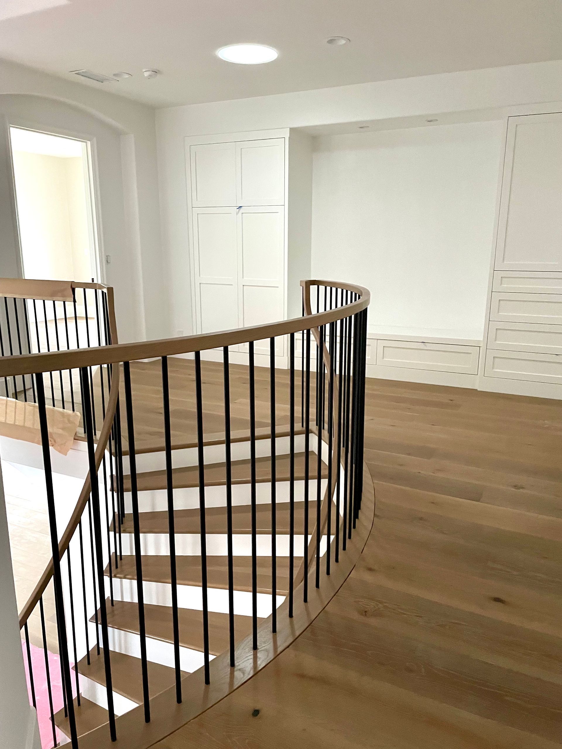 Curved wooden staircase with black iron spindles, leading to a bright white upper level.