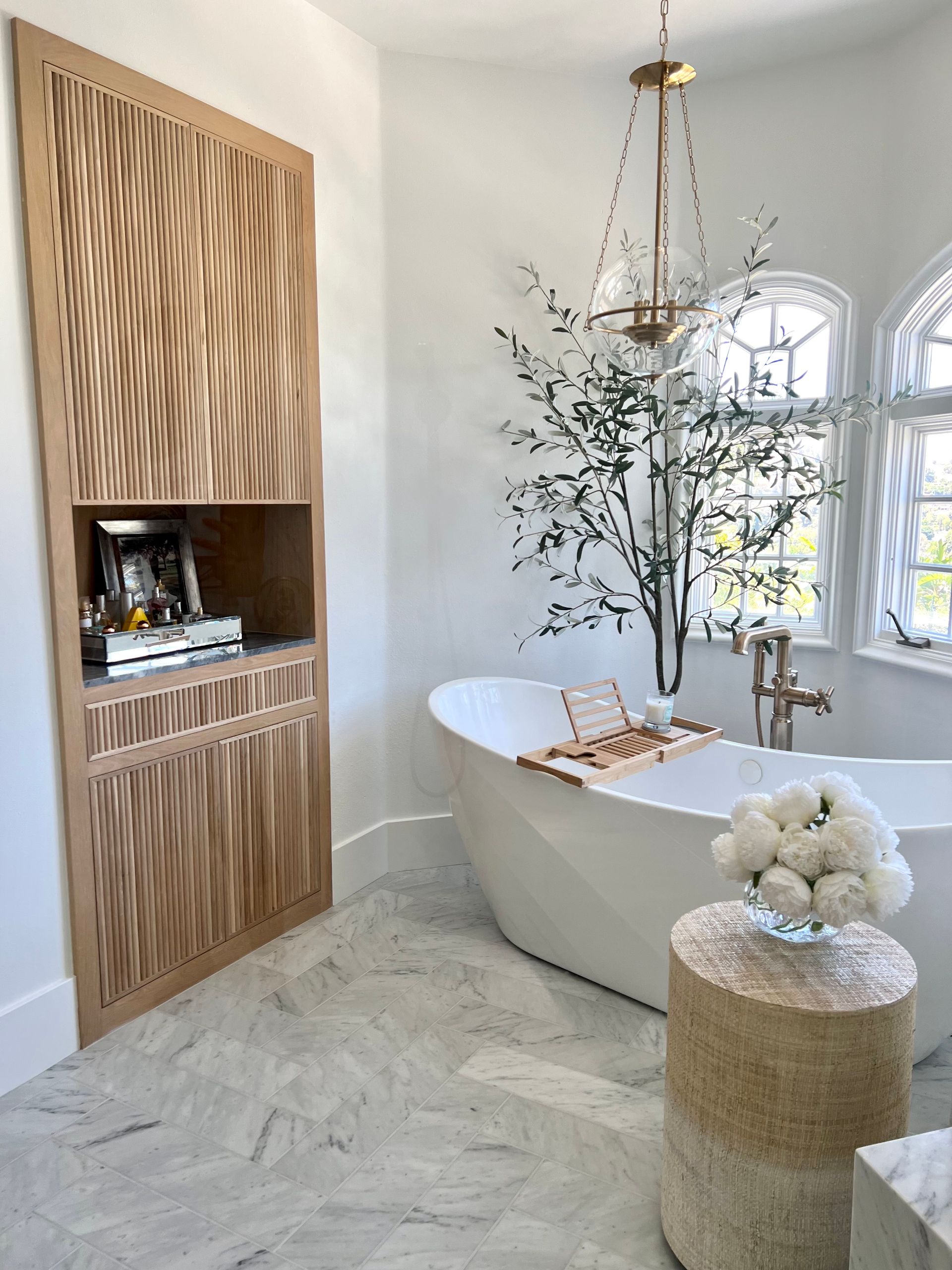 Bathroom with a freestanding tub, wood storage cabinet, and marble flooring.