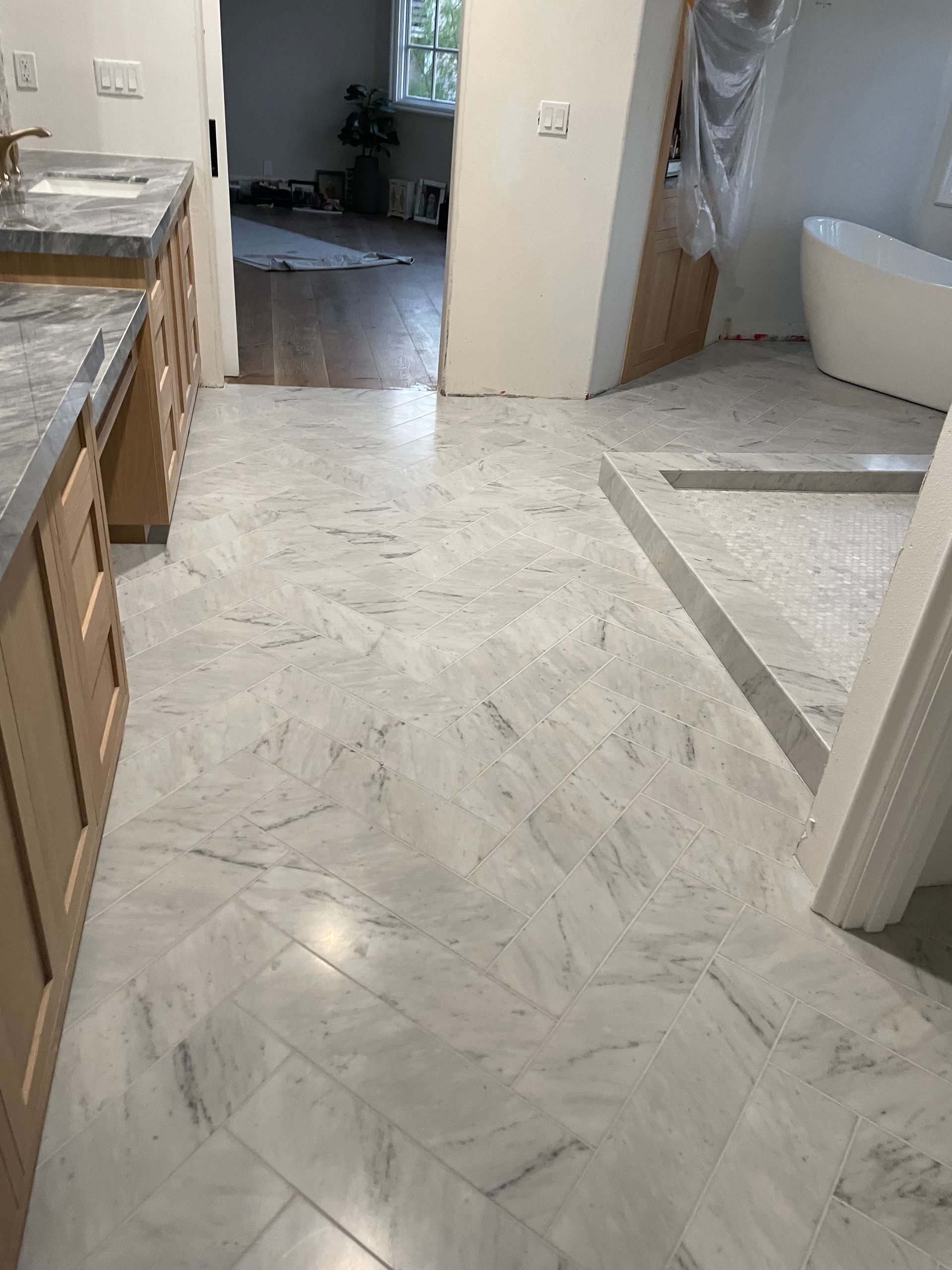 Bathroom with light gray and white patterned tile flooring. Wooden cabinetry and a bathtub are visible.