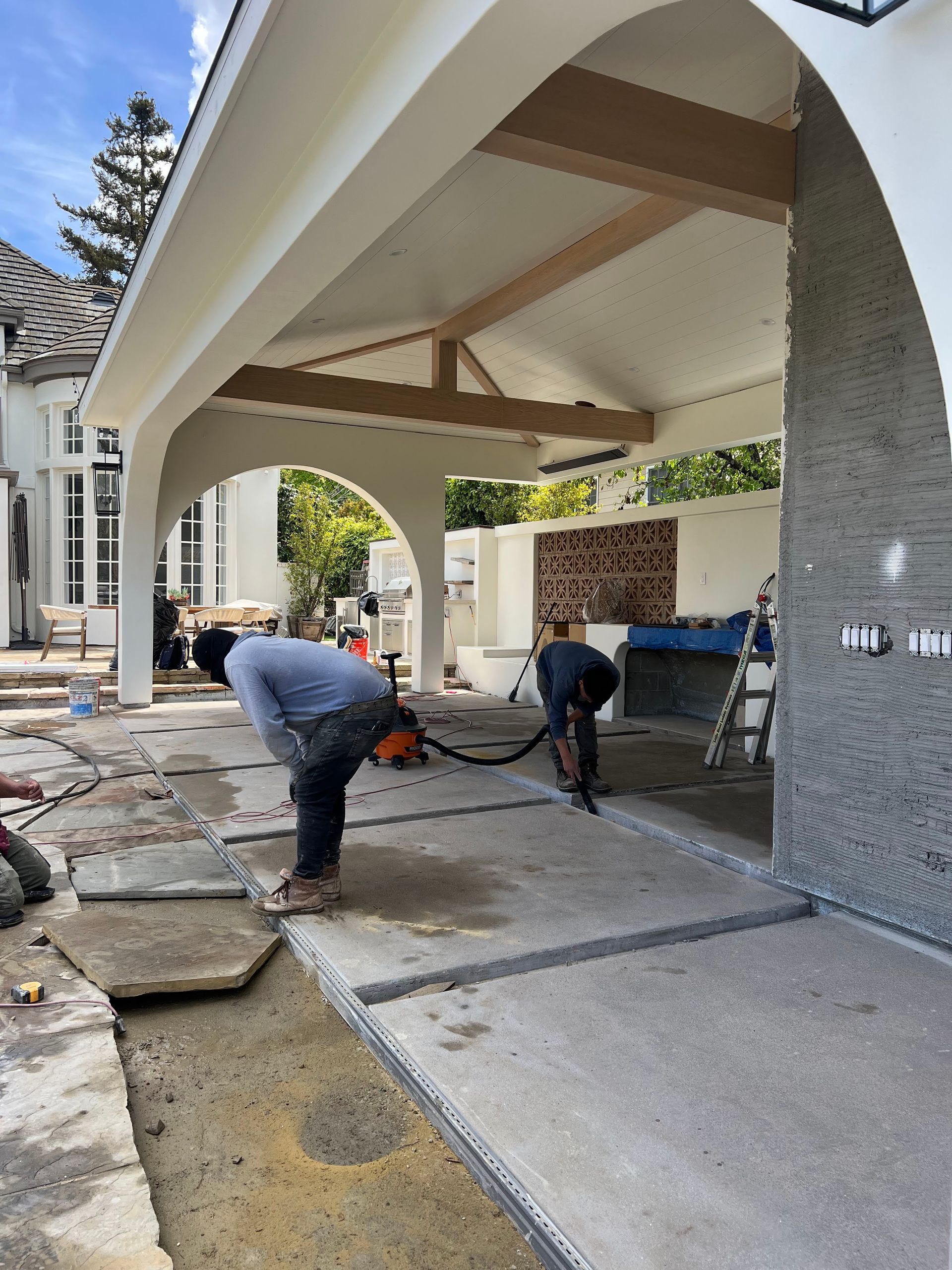 Two construction workers cleaning concrete slabs under a covered patio.