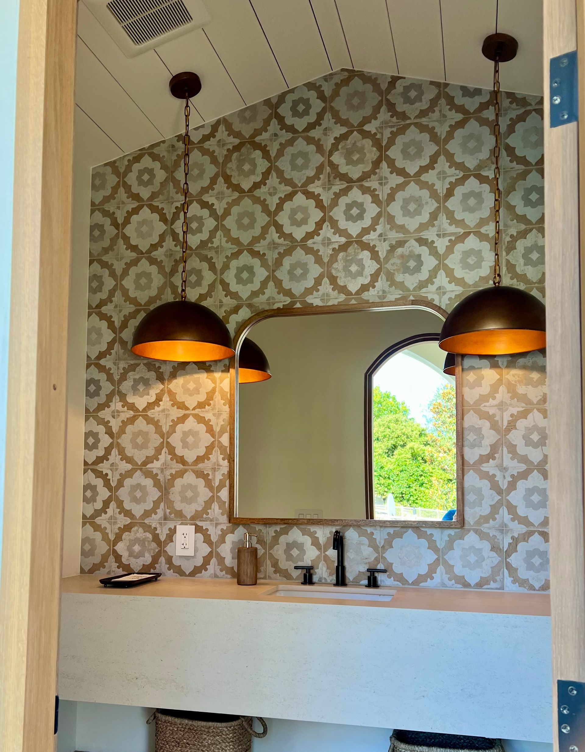 Bathroom with patterned tile wall, arched mirror, pendant lights, and built-in sink.