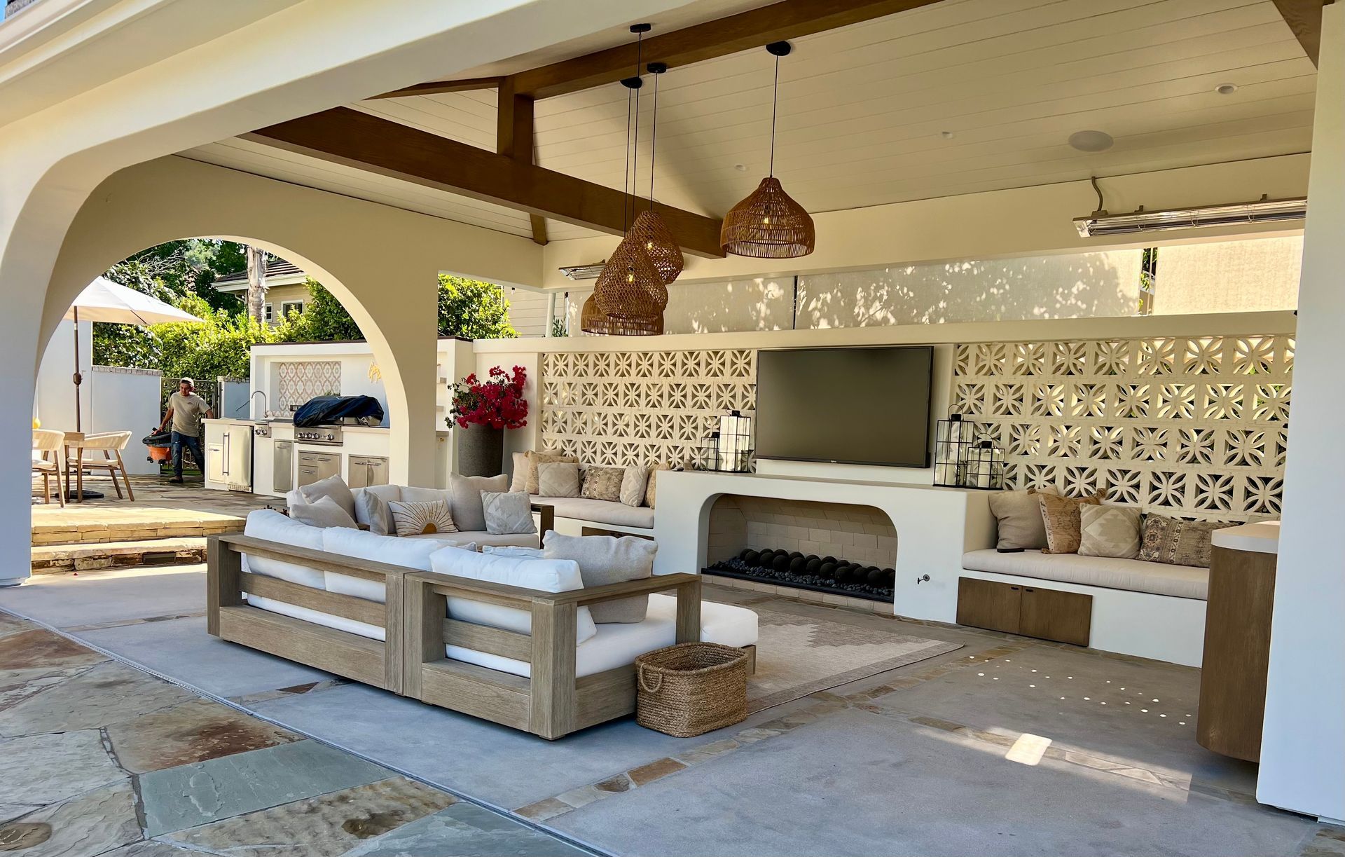 Outdoor patio with seating, fireplace, and patterned wall, under a covered area with wooden beams.