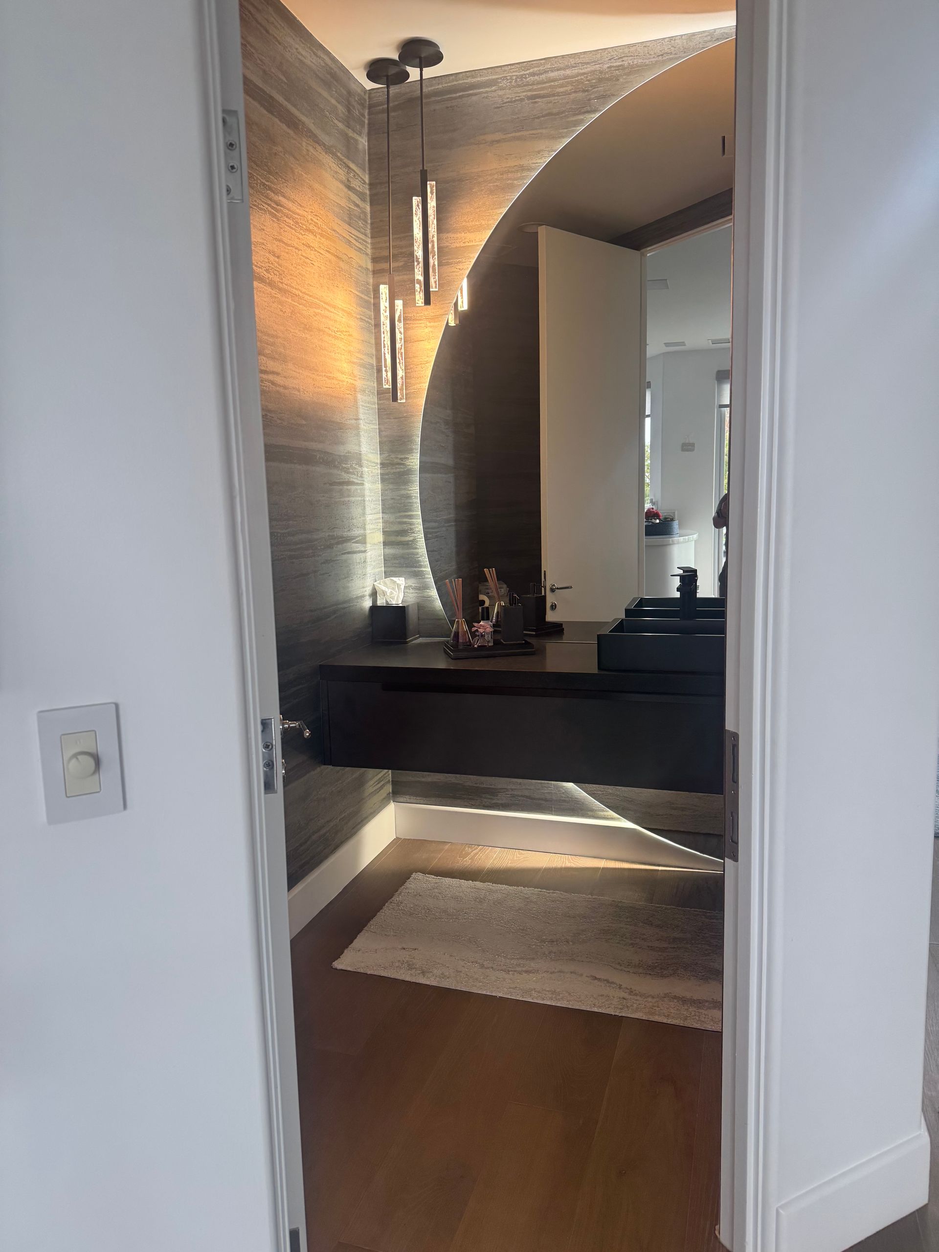 Hallway entrance to a room with a decorative accent wall, a floating dark wood desk, and pendant lights.