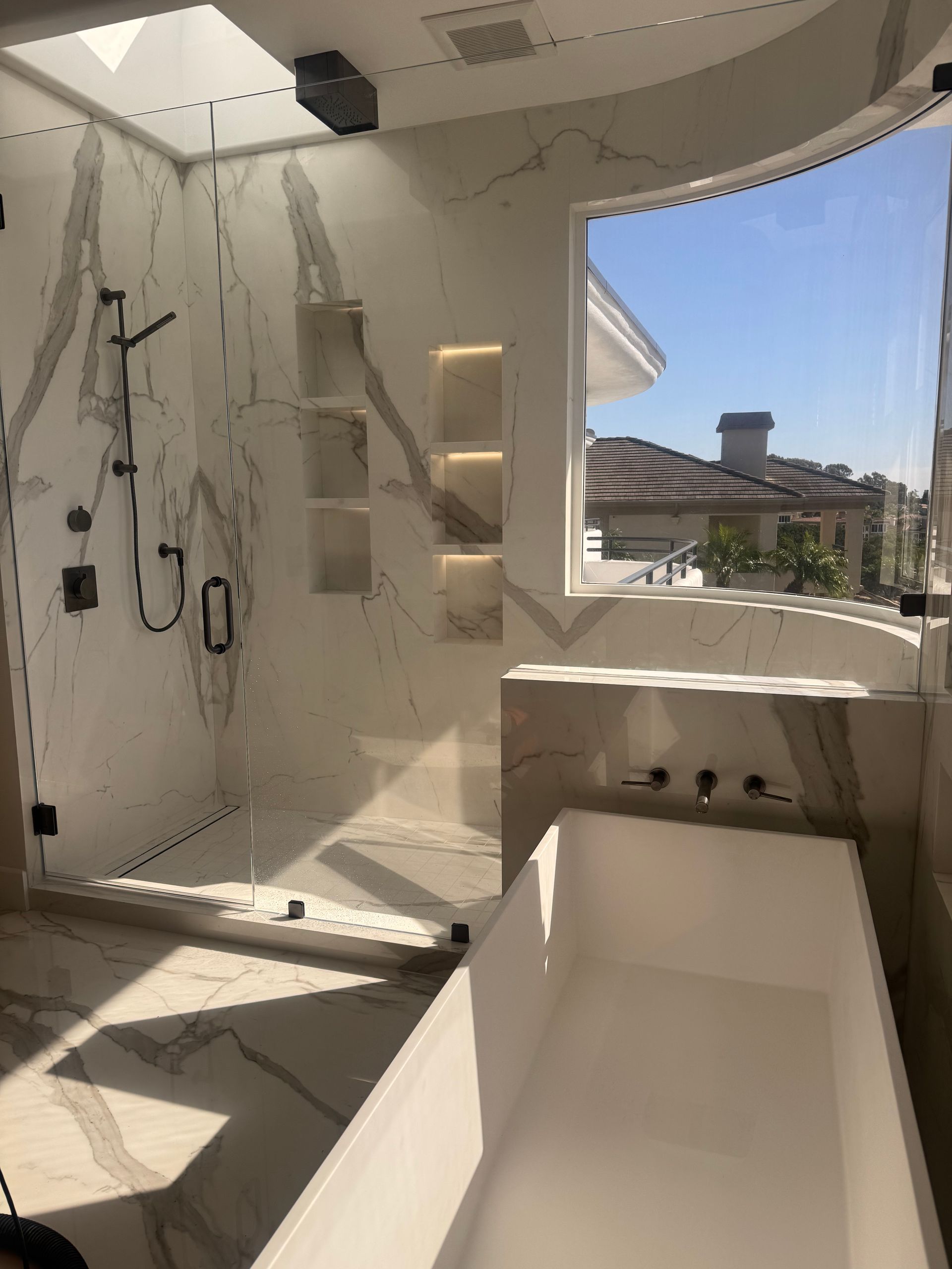 Luxurious bathroom with marble shower, soaking tub, and window overlooking a sunny outdoor scene.