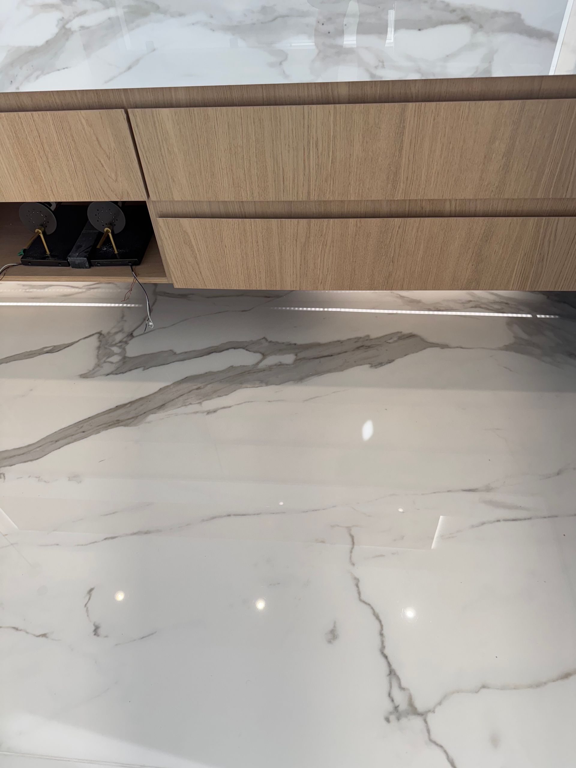 Light oak cabinets over white marble-look flooring with gray veining.