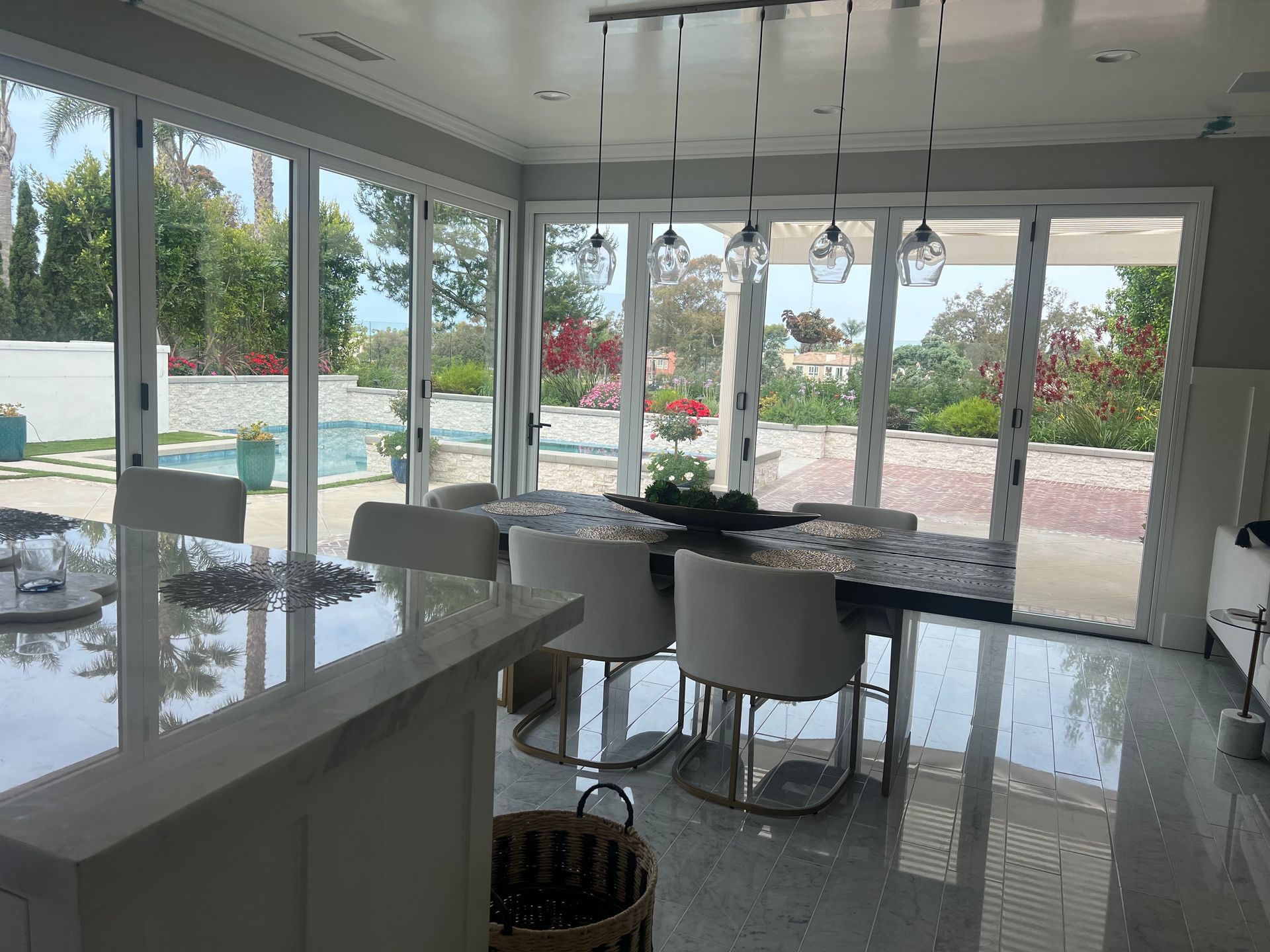 Modern dining room with a long table, chairs, and large glass doors leading to a pool and garden.