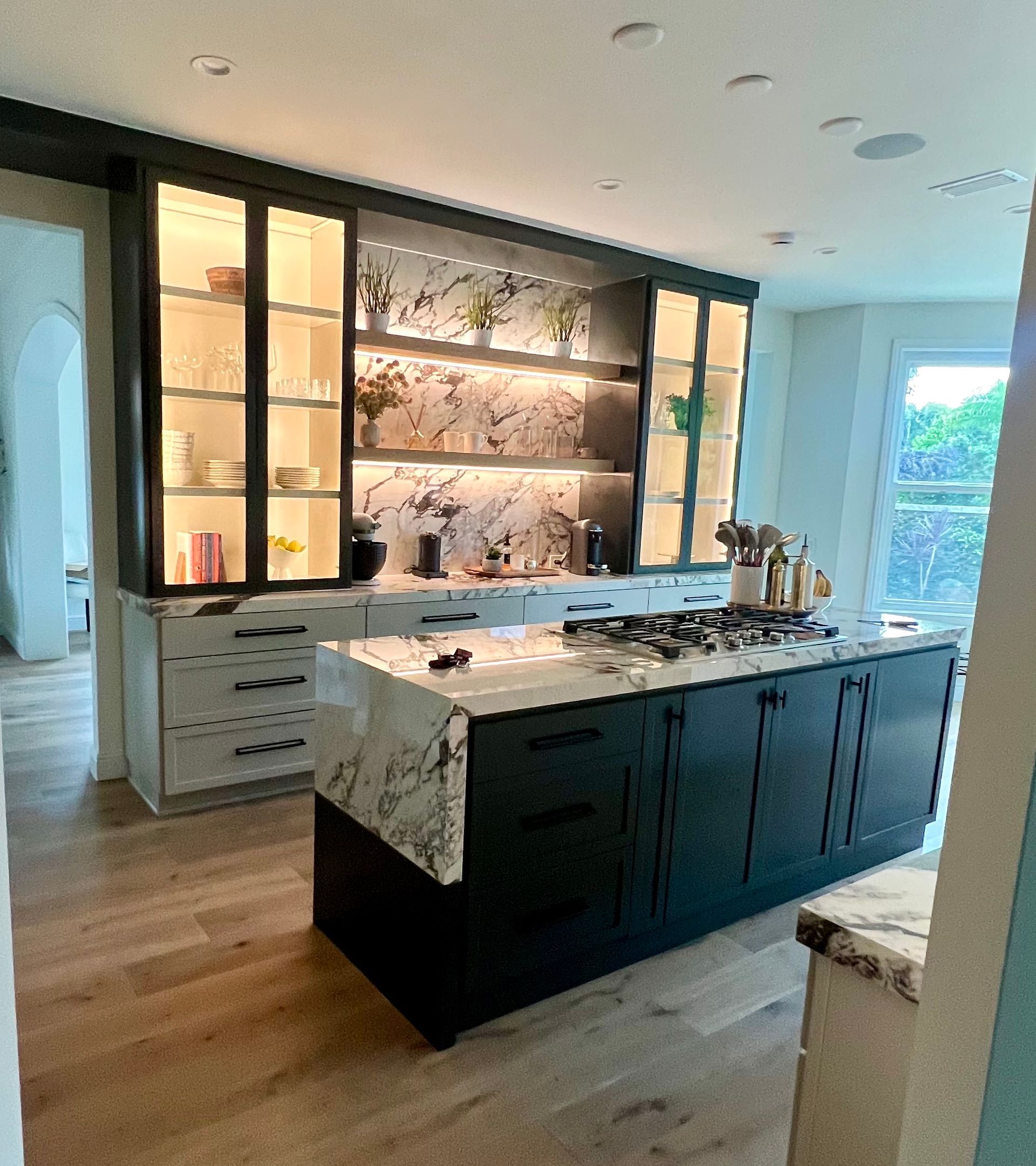 Kitchen with dark green cabinets, marble countertops, and built-in glass display shelves with lights.