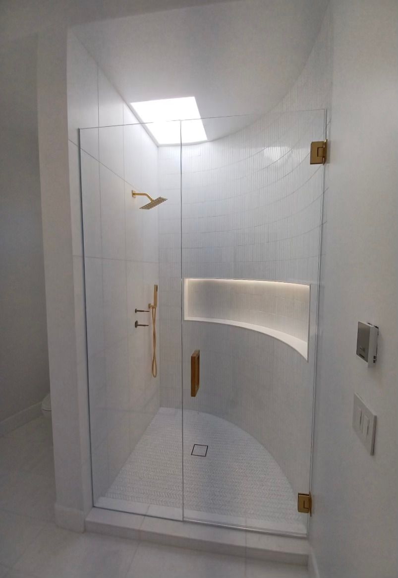 Modern shower with glass door, gold hardware, white tile, and a skylight.