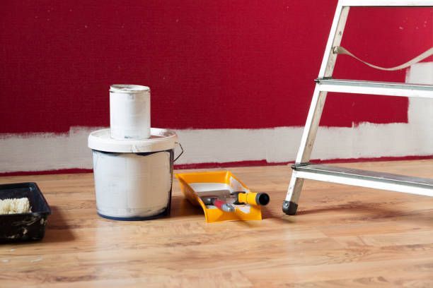 A bucket of paint is sitting on the floor next to a ladder.