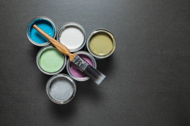 A bunch of cans of paint and a brush on a table.