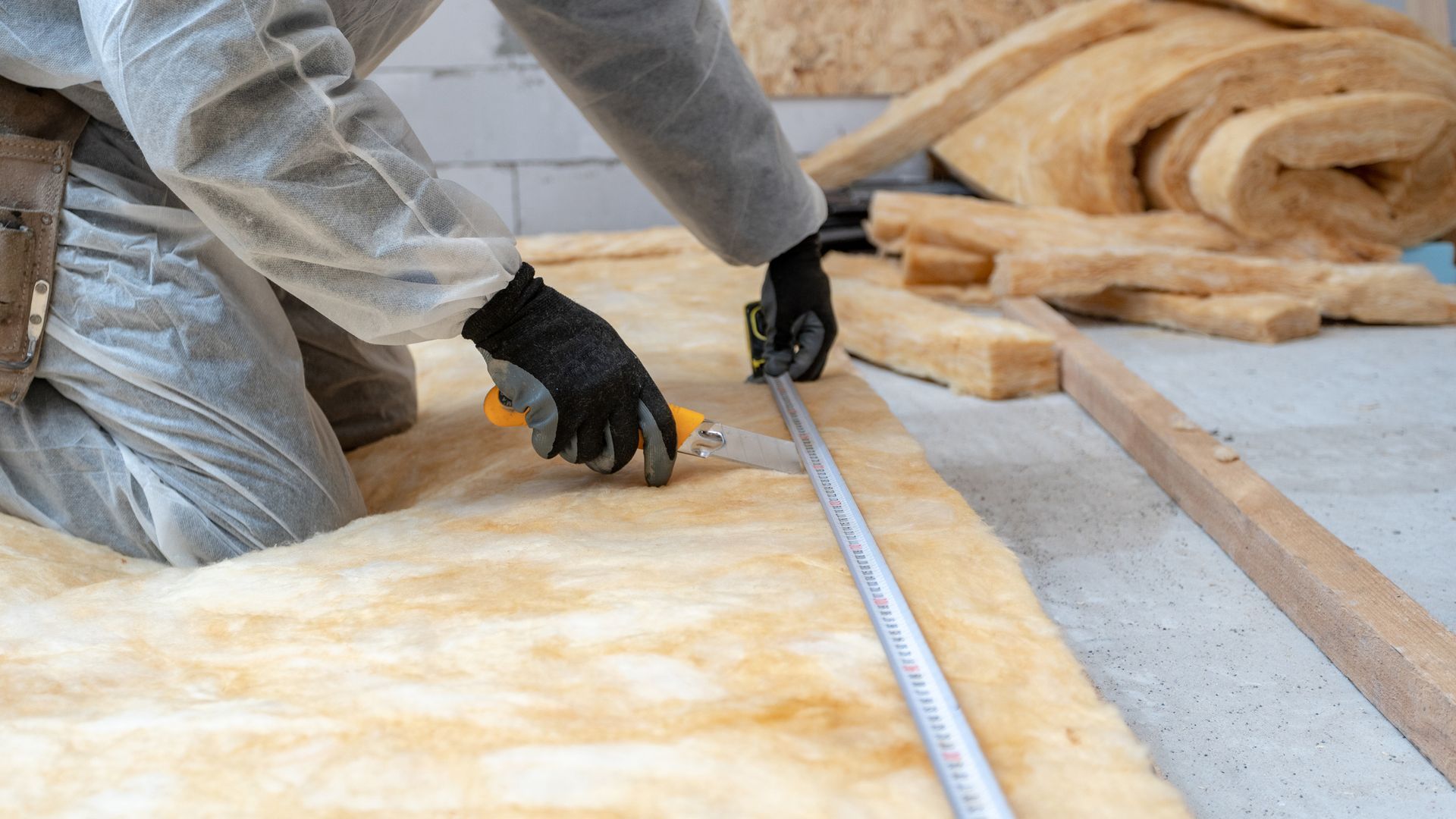 A man is measuring a piece of insulation with a tape measure.