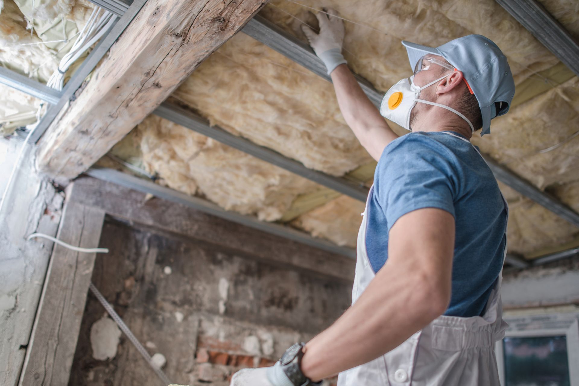 A man wearing a mask is insulating the ceiling of a building.