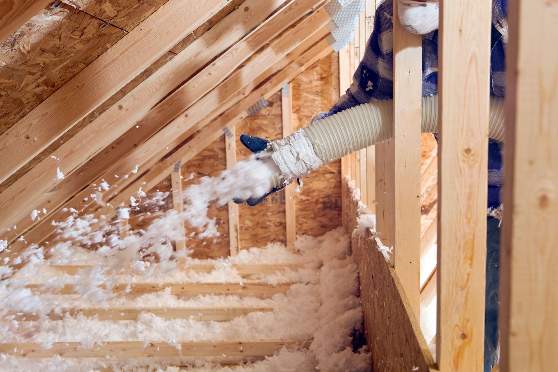 A person is blowing insulation into the attic of a house under construction.