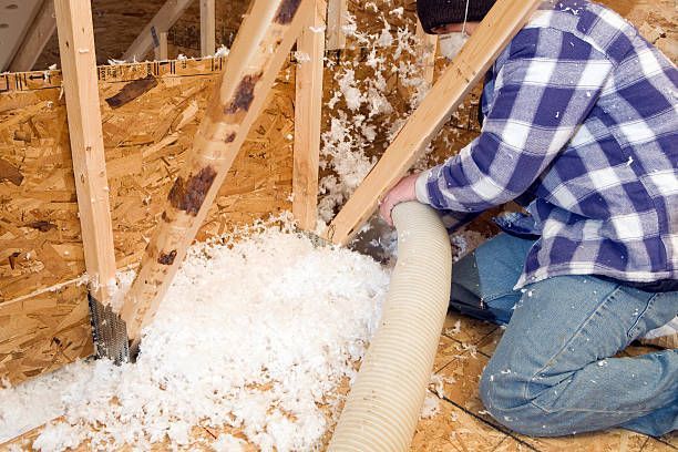 A man is blowing insulation into the attic of a house.