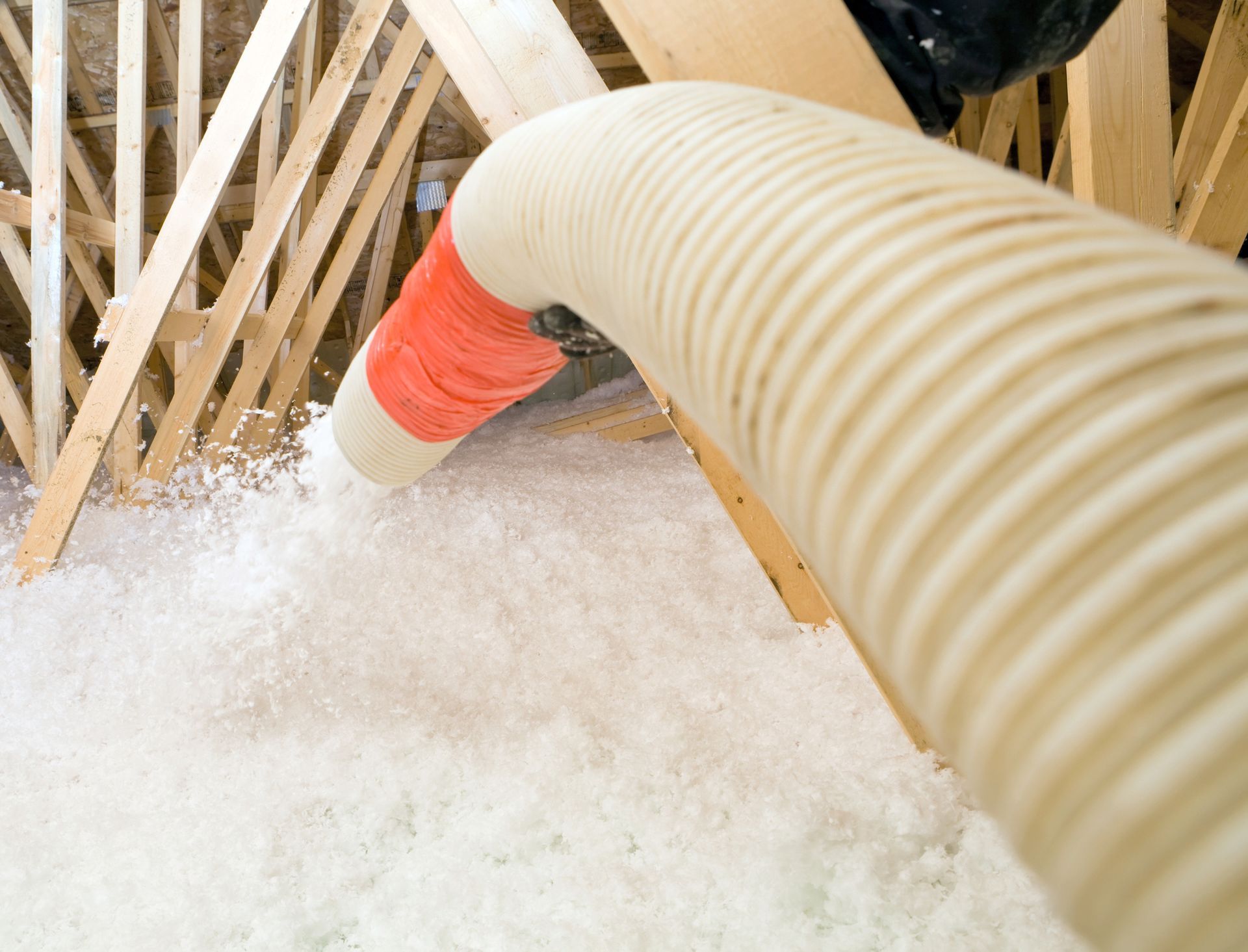 A hose is being used to blow insulation into an attic