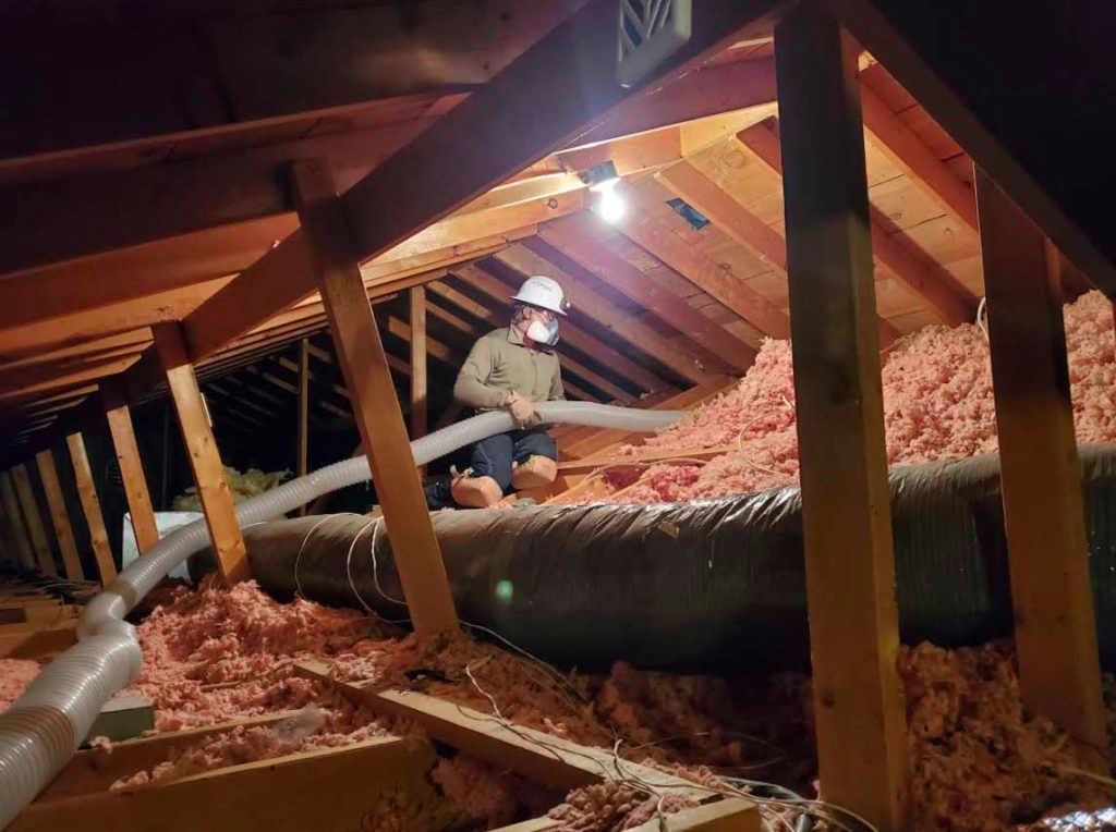 A man is blowing insulation into an attic with a vacuum hose.