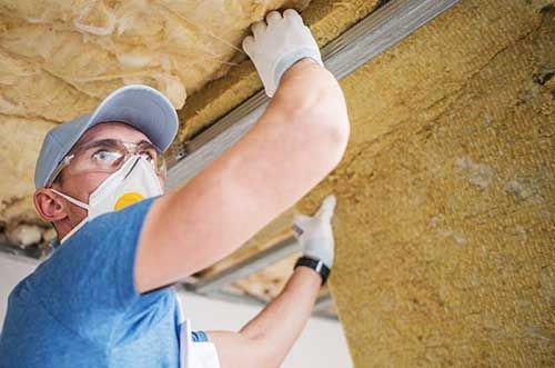 A man wearing a mask and gloves is working on a ceiling.