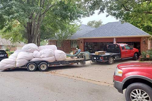 A red truck is towing a trailer full of bags in front of a house.