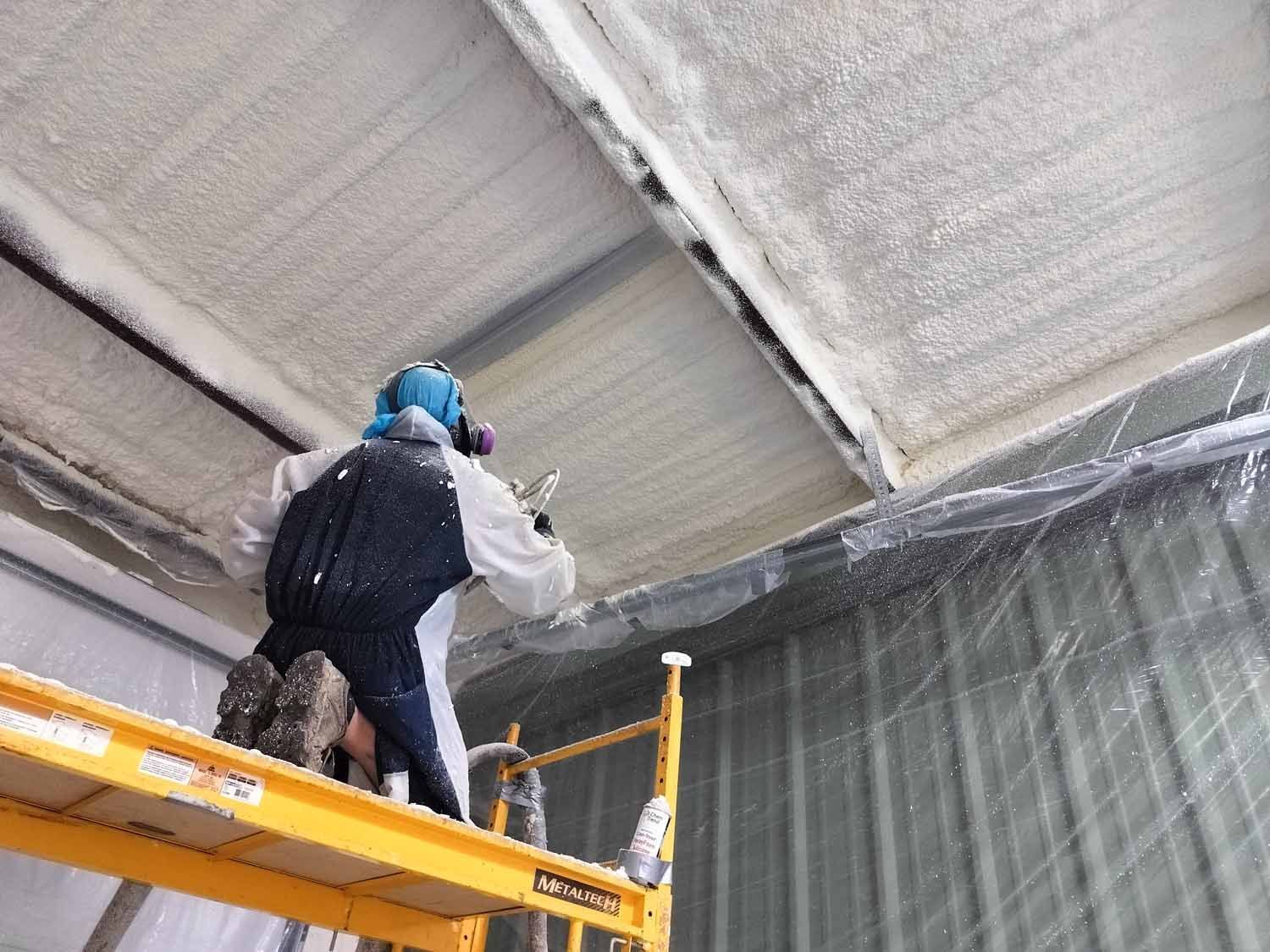 A man is spraying foam on the ceiling of a building.
