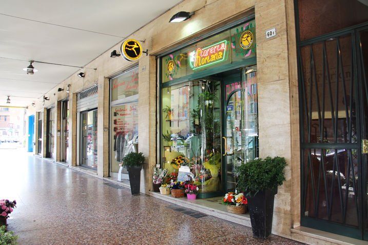 Vista di negozi dalla strada. Negozio di fiori con insegna gialla, piante in vaso all'ingresso.