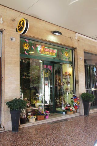 Vetrina di un negozio di fiori con tenda verde, fiori dai colori vivaci e un'insegna al neon.