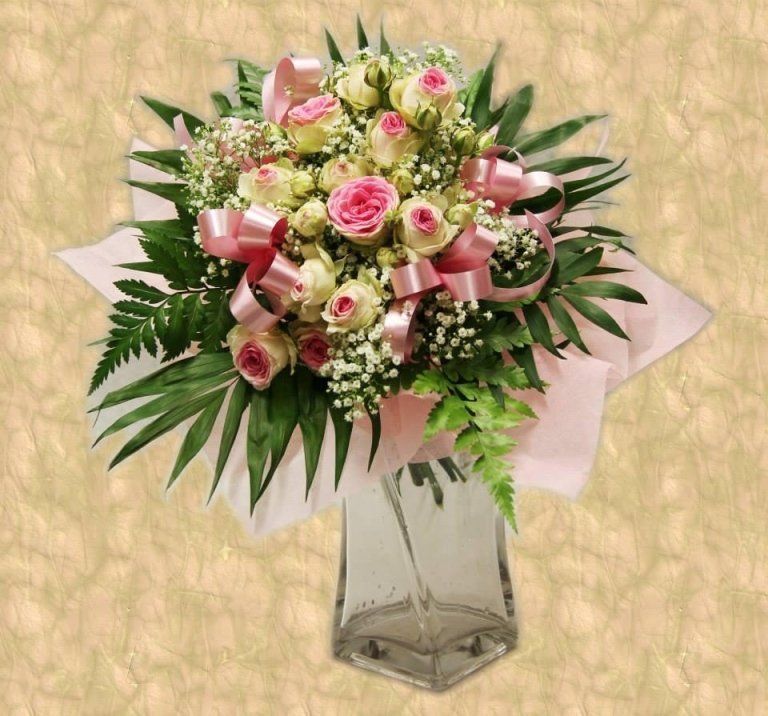 Bouquet di rose rosa e bianche con un nastro rosa in un vaso trasparente su una superficie decorata.