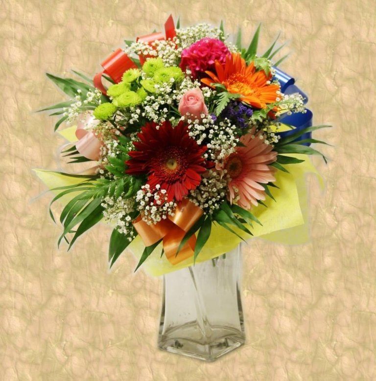 Mazzo di fiori colorati in un vaso trasparente con nastri, su uno sfondo strutturato.