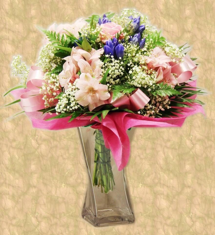 Bouquet di fiori rosa e blu in un vaso di vetro, avvolto in tessuto rosa e nastro.