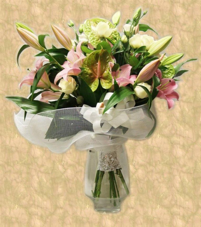 Bouquet di gigli rosa e rose bianche in un vaso di vetro, avvolto in una rete, su uno sfondo beige.