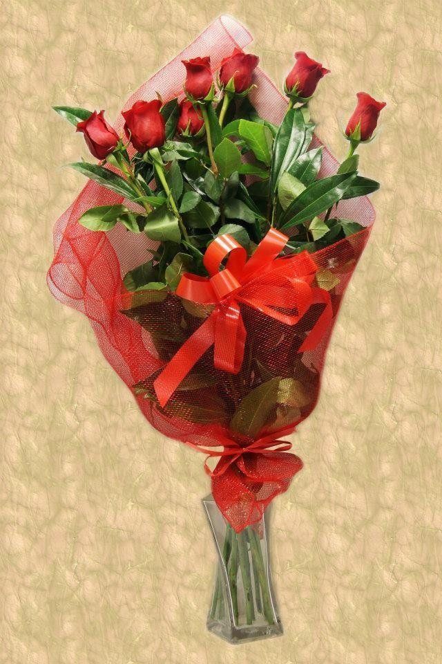 Bouquet di rose rosse avvolto in una rete rossa con un fiocco rosso, in un vaso trasparente.