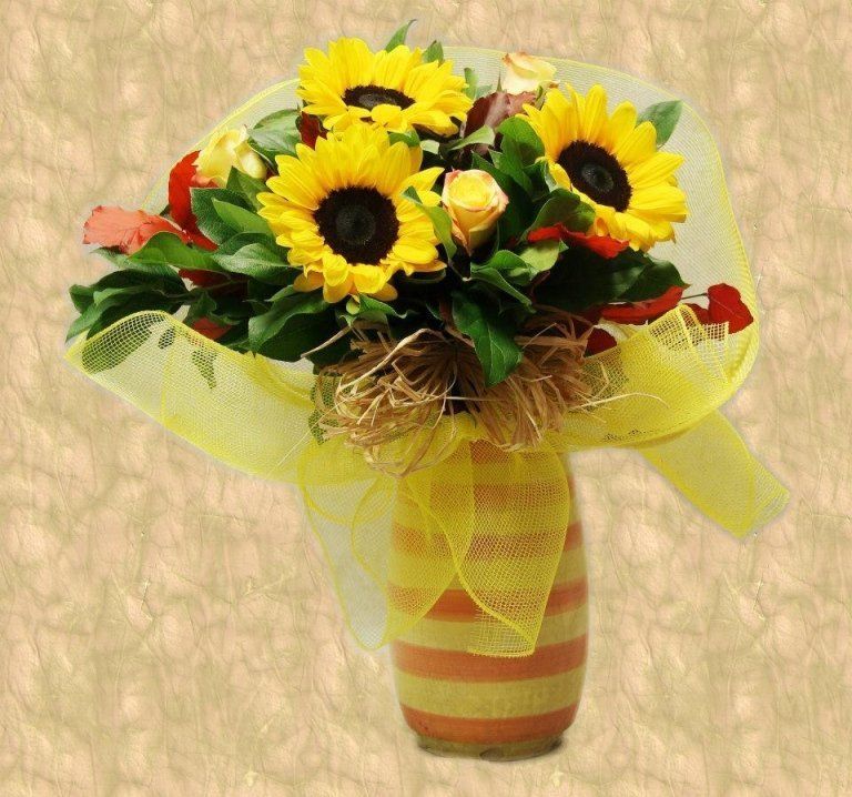 Mazzo di girasoli, rose e verde in un vaso giallo a righe, avvolto in una rete gialla.