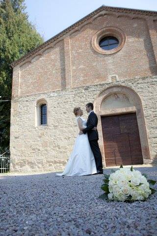 Gli sposi si abbracciano davanti a una chiesa in mattoni; bouquet bianco a terra.