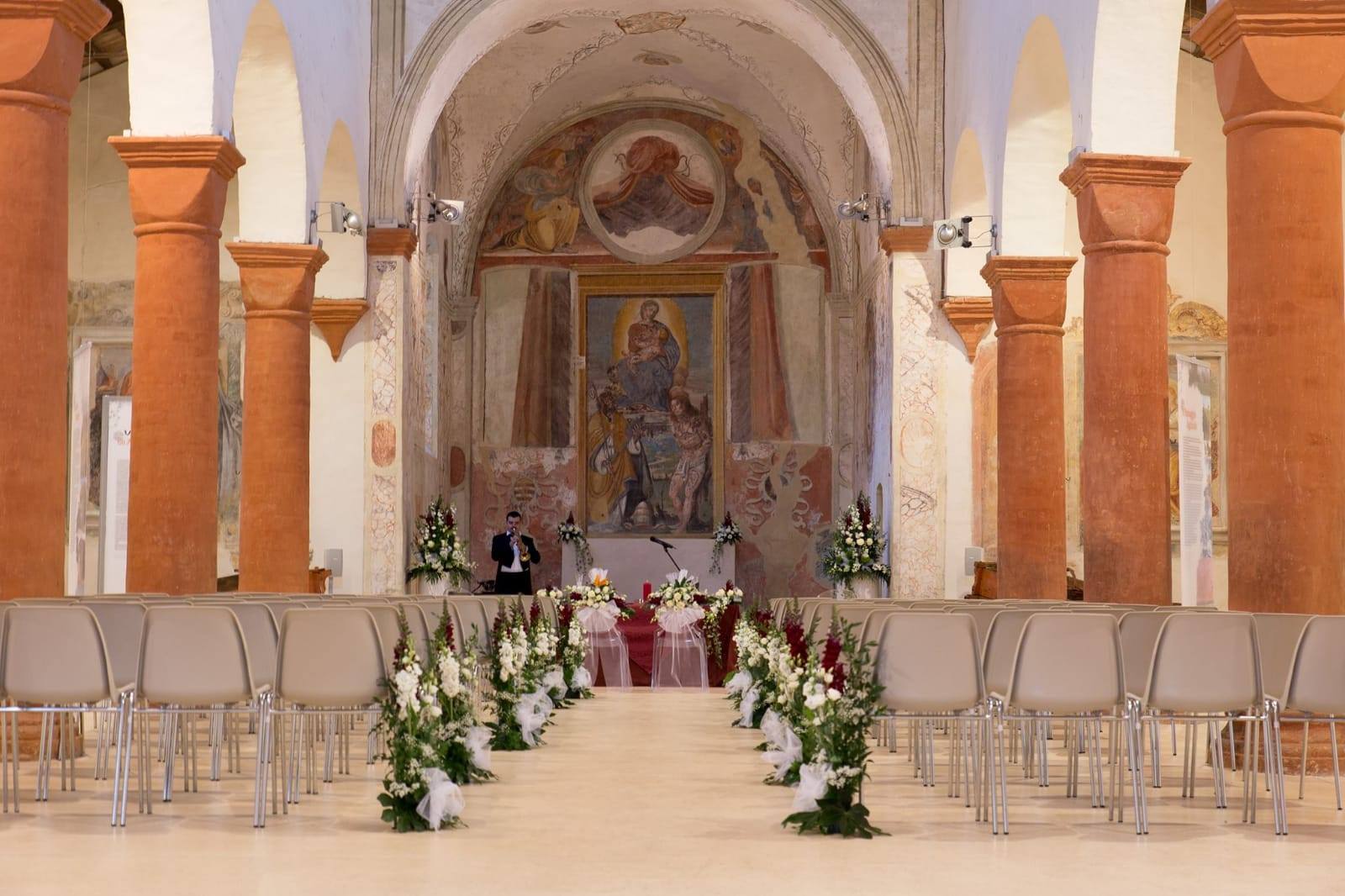 Cerimonia nuziale in chiesa con file di sedie, decorazioni floreali lungo la navata e un altare.