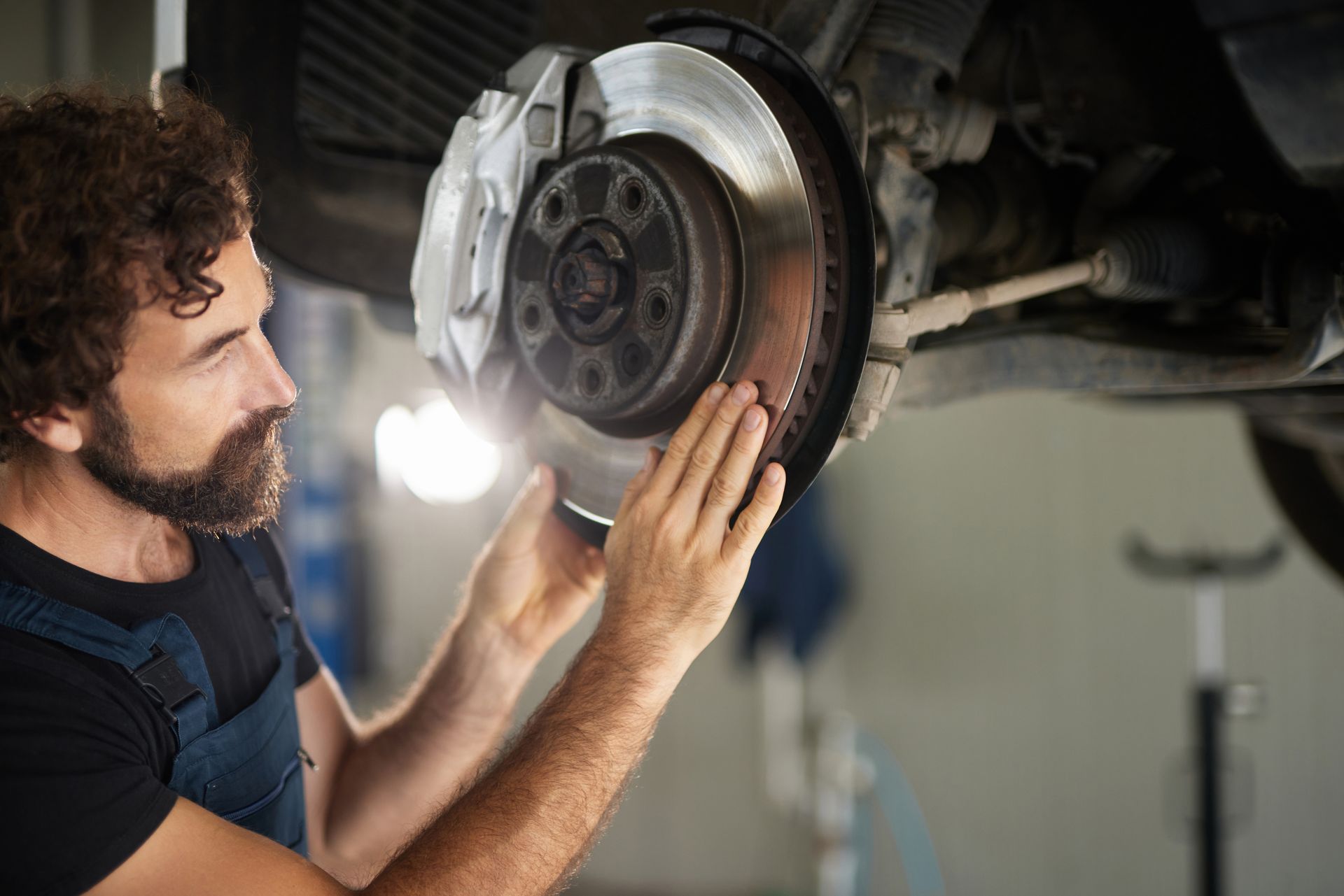 A car mechanic focuses on inspecting and repairing the brake system of a vehicle in a garage space.