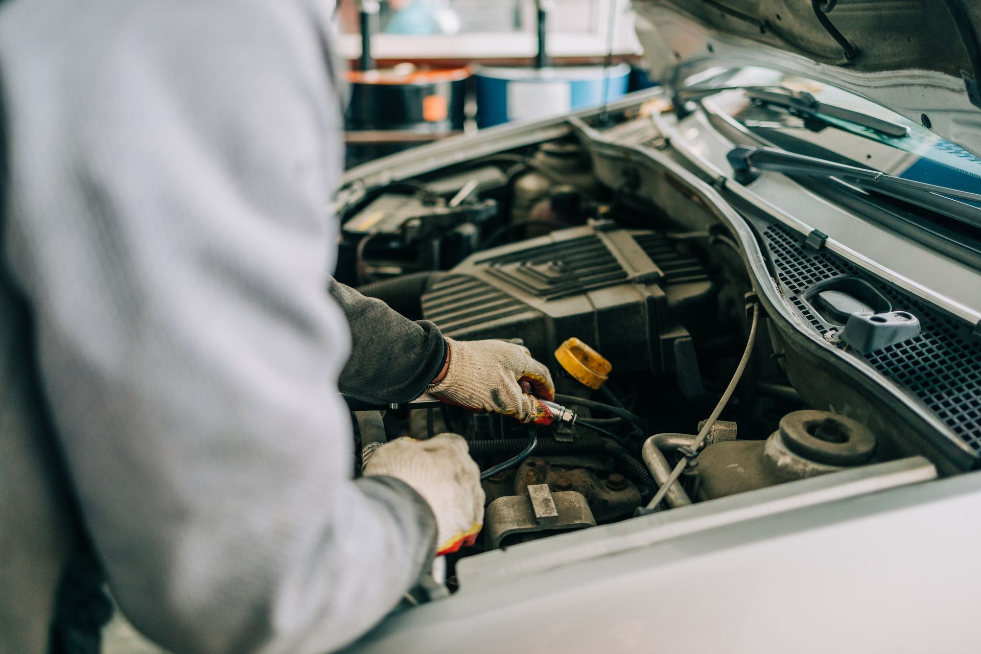 A mechanic using tools to fix a car engine in an auto repair shop.