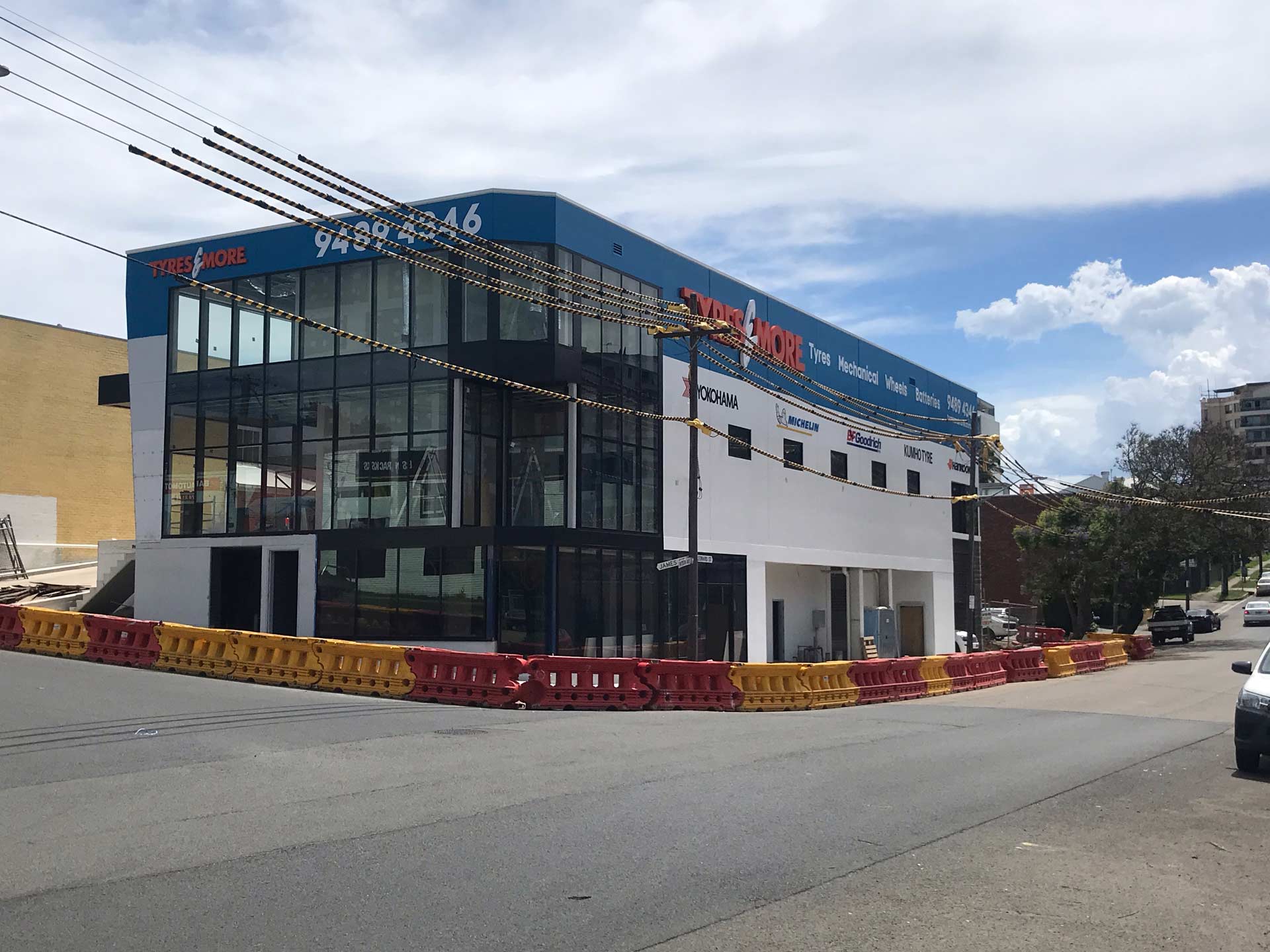 Modern two-story building on a corner lot, blue and white facade, large windows, construction barriers.