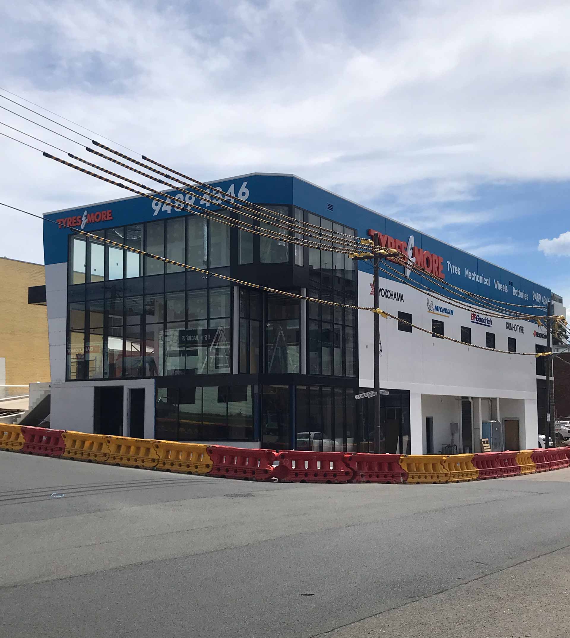 Two-story commercial building with blue trim, glass facade, white walls, and a parking barrier.