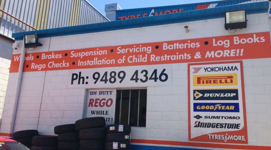 Exterior of a tire shop with a white and orange facade, services listed, phone number, and tire brands.
