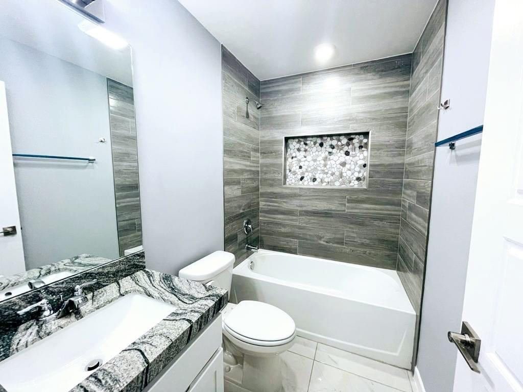 Close-up of a kitchen countertop with marble-like veining, overlooking a kitchen with gray cabinets and a window.