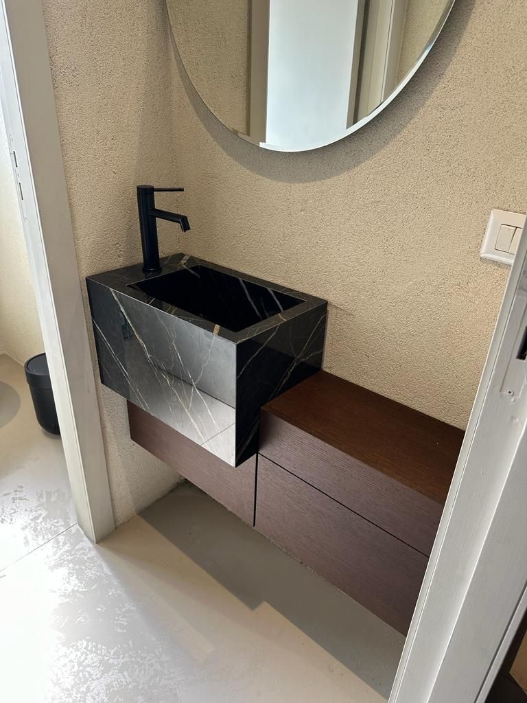 Un bagno con un lavandino nero e uno specchio rotondo.